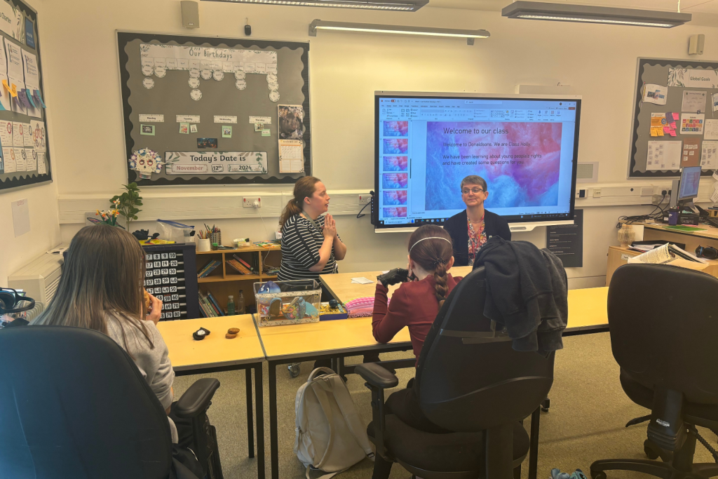 Maggie sitting next to Class Holly teacher Rebekah engaging in conversation with two young people.